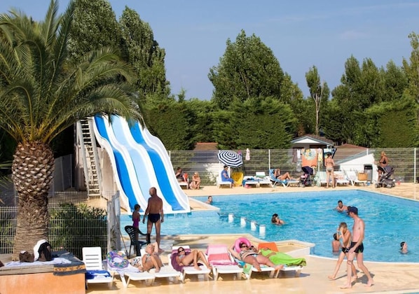 Ein Swimmingpool mit Rutsche, Palmen und Menschen, die am Pool entspannen.