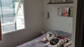 Un dormitorio con una cama, una ventana, una estantería con adornos y una pared con tablas de surf.