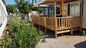 Une terrasse en bois dotée d’un espace salon couvert, entourée de verdure et délimitée par une clôture.