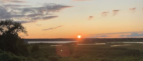 A sunset over a grassy field with a path leading towards a body of water.