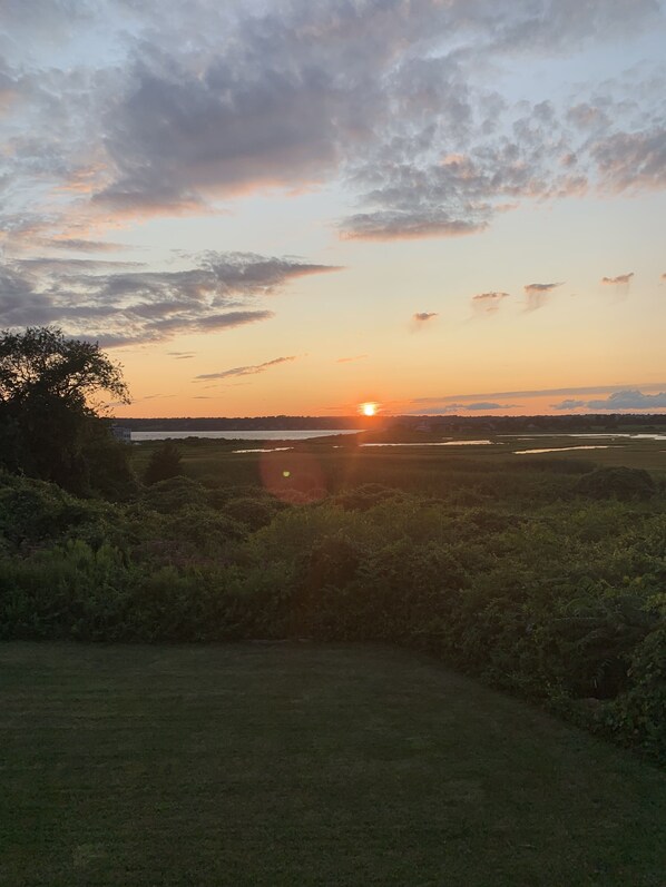 A sunset over a grassy field with a path leading towards a body of water.