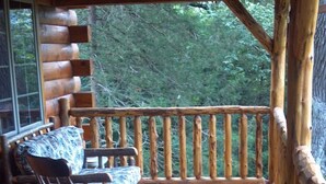 A wooden deck with a rocking chair and a table, overlooking a forested area. - Root River Valley Cabin ~ Lanesboro, MN (Lanesboro)