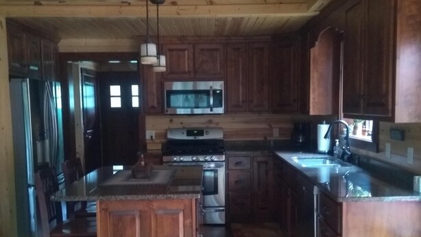 A wooden cabin interior with a kitchen area, including a refrigerator, stove, microwave, and wooden cabinets. - Root River Valley Cabin ~ Lanesboro, MN (Lanesboro)