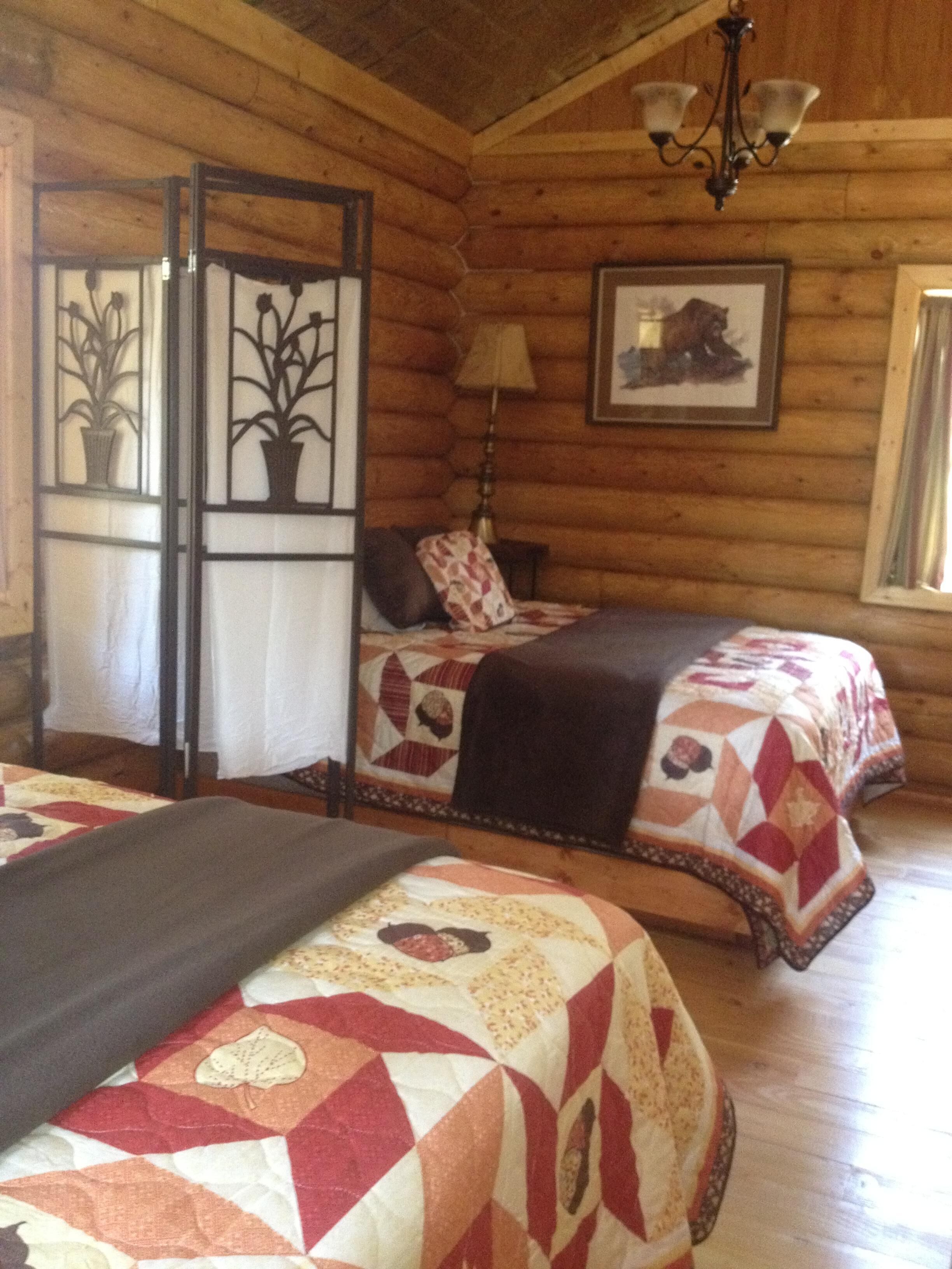 Acogedora habitación tipo cabaña de madera con dos camas, un candelabro y una ventana con cortinas.