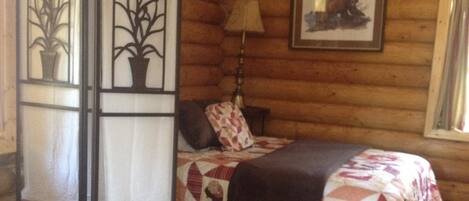 Acogedora habitación tipo cabaña de madera con dos camas, un candelabro y una ventana con cortinas.