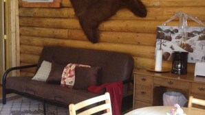 A cozy room with a wooden log wall, a brown leather couch, a dining table with chairs, and a mounted fur rug.