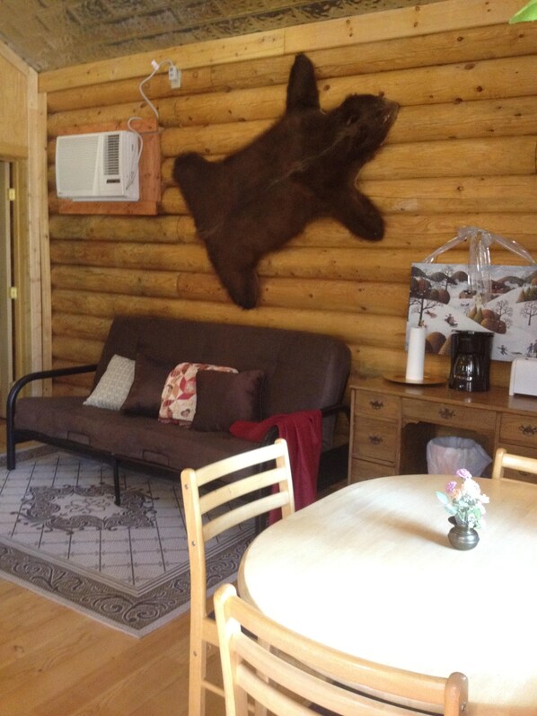 Una habitación acogedora con pared de troncos de madera, un sofá de cuero marrón, una mesa de comedor con sillas y un manto de piel.
