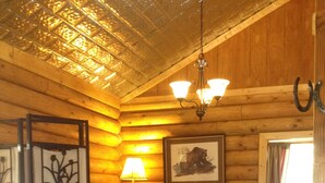 A cozy log cabin room with two beds, a lamp, a framed picture, and a window with curtains.