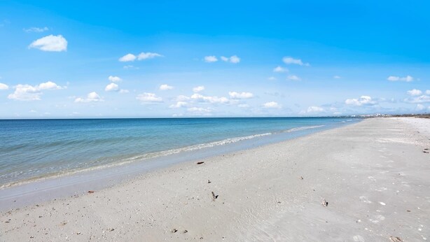 Ein weiter Sandstrand mit sanften Wellen, einem klaren Himmel und einem entfernten Steg.