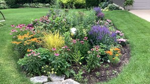 A well-maintained garden with a variety of flowers and shrubs, a stone border, and a lawn. - A Pleasant Retreat (Sun Prairie)