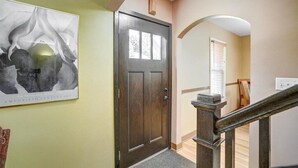 Un couloir avec une porte en bois sombre, un tableau abstrait encadré et un escalier doté d’une rampe en bois.