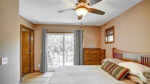 A bedroom with a bed, a ceiling fan, a dresser, and a window with curtains. - A Pleasant Retreat (Sun Prairie)