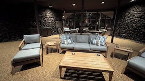 Un espace extérieur aménagé avec un canapé, des fauteuils et des tables, entouré de murs en pierre et agrémenté d’une cheminée en pierre.
