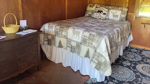 Ein Schlafzimmer einer Holzhütte mit einem Bett, einem Nachttisch, einem Korb und einem Fenster.