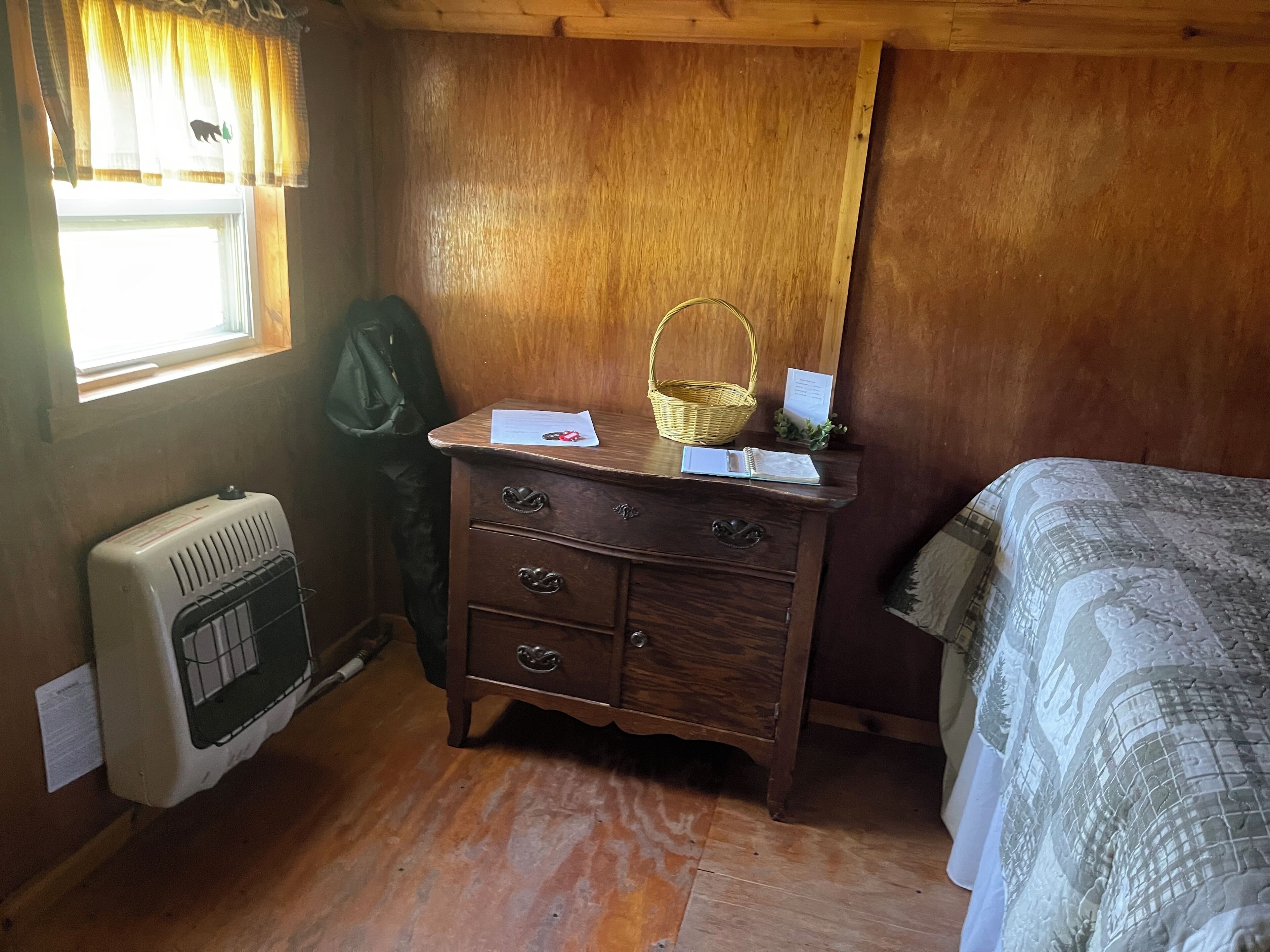 Une pièce en bois avec un lit, une commode à tiroirs, un radiateur et une fenêtre avec des rideaux.