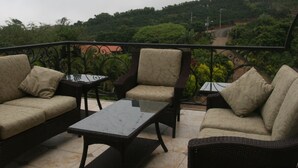 Un balcón con mobiliario de mimbre, incluyendo dos sofás y una mesa, con vistas a un paisaje verde exuberante.