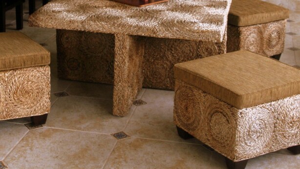 Una habitación con un sofá y reposapiés de tejido trenzado, una mesa de centro a juego y una zona de bar con taburetes.