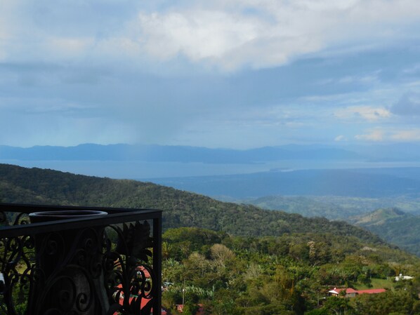 A scenic view from a balcony overlooking a mountainous landscape with lush greenery and distant hills.