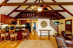 A spacious loft-style living area with a kitchen, wooden ceiling beams, a ceiling fan, and a staircase leading to an upper level. - Sweet Refrain in Pisgah Forest with VIEW (PIsgah Forest)