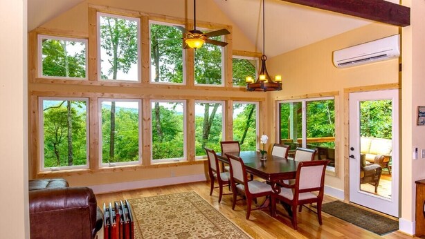 A dining area with a wooden table and chairs, large windows with a forest view, a ceiling fan, and an air conditioning unit. - Sweet Refrain in Pisgah Forest with VIEW (PIsgah Forest)