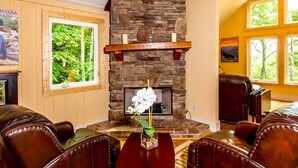 A cozy room with a stone fireplace, leather chairs, and a large window with a forest view. - Sweet Refrain in Pisgah Forest with VIEW (PIsgah Forest)