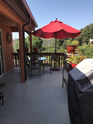 A covered patio with a table and chairs, a red umbrella, and potted plants.