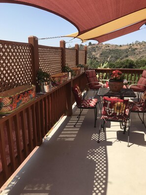 A covered outdoor patio with a wooden fence, red and white patterned chairs, and potted plants.