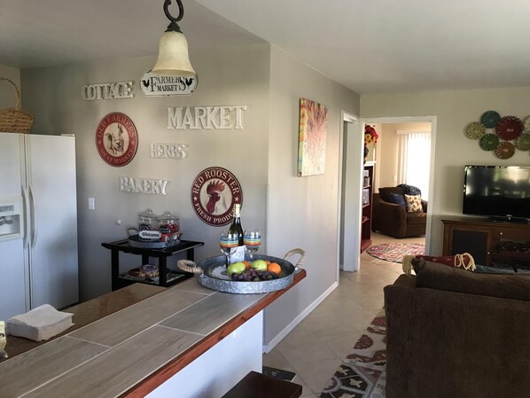 A modern kitchen with a central island, a refrigerator, and a dining area with a sofa and a TV.