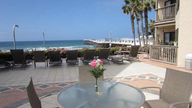 A patio with a glass table and chairs, overlooking a beach with palm trees and a pier. - Ocean View 2 Bdrm / 2 Bath Beach Condo in San Diego (Pacific Beach) (San Diego)