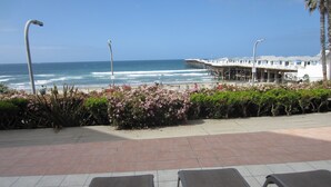 A beachside view with lounge chairs, a pier, and a building with balconies. - Ocean View 2 Bdrm / 2 Bath Beach Condo in San Diego (Pacific Beach) (San Diego)