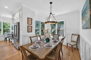 A dining area with a wooden table set for six, surrounded by chairs, with a chandelier above.