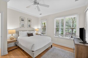 Une chambre à coucher comprenant un lit, des tables de chevet, un ventilateur de plafond, une télévision et une fenêtre avec des stores.