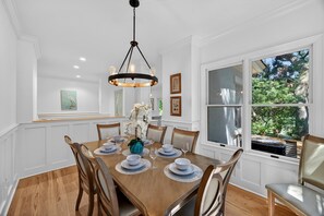 Une salle à manger avec une table en bois dressée pour six personnes, entourée de chaises, d’un lustre et d’œuvres d’art encadrées accrochées aux murs.
