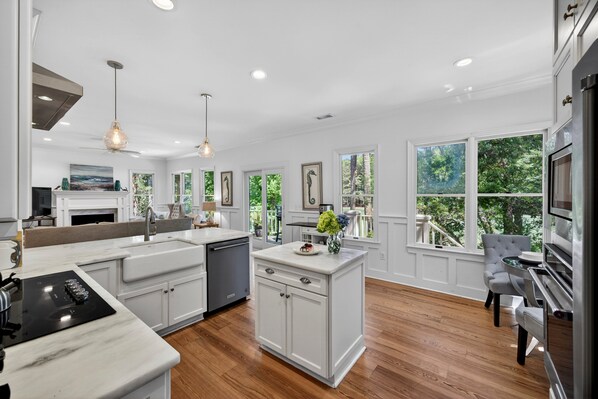 A spacious kitchen with white cabinetry, a central island, and large windows offering views of greenery.