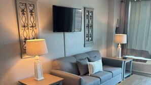 En moderne stue med en grå sofa, et sofabord, et fjernsyn ophængt på væggen og en lampe på et sengebord.