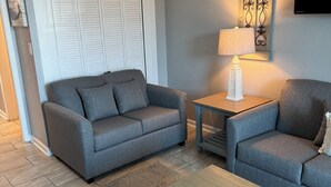 En stue med en grå sofa, en matchende lænestol, et lille bord med en lampe og et træsofabord.