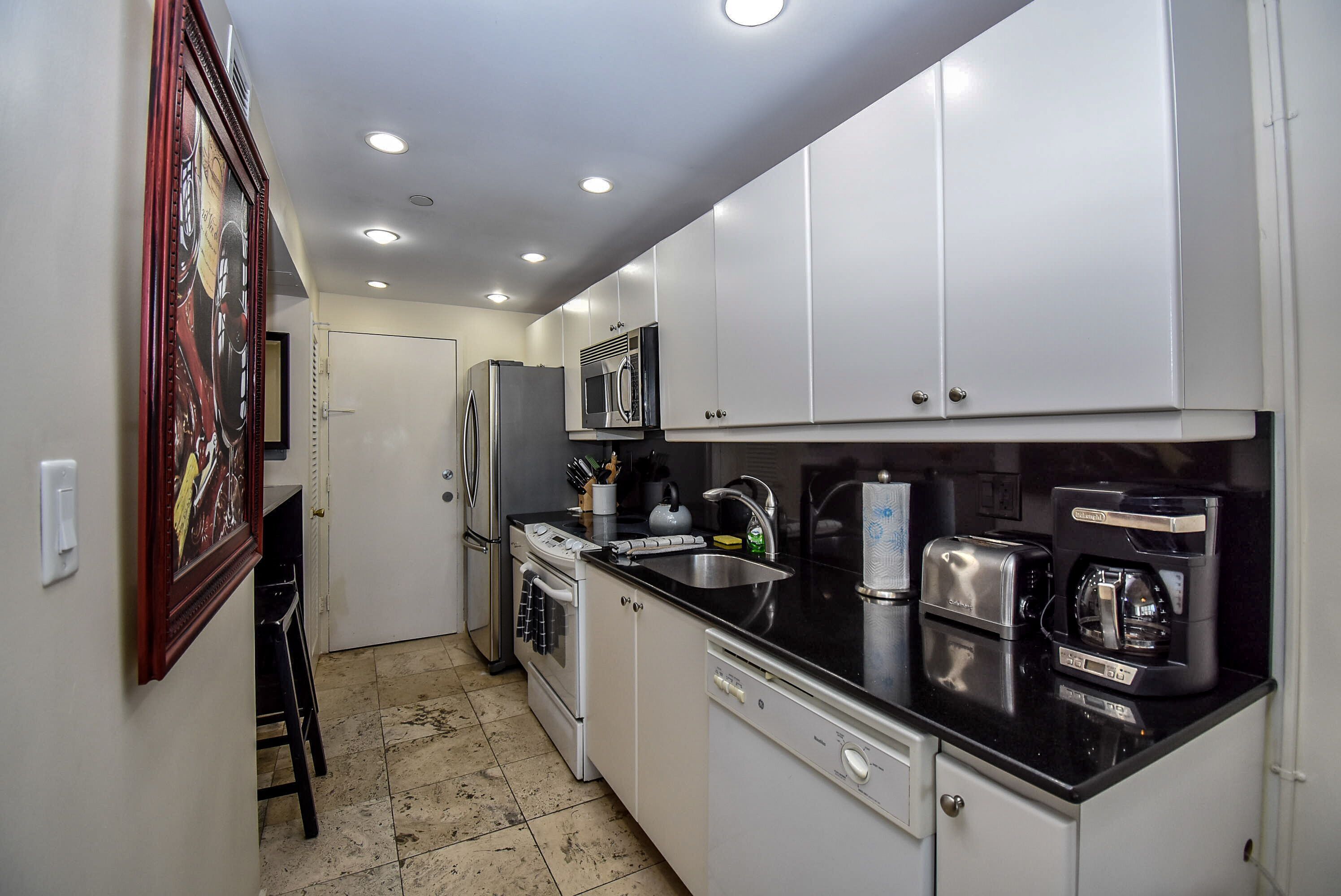 A compact kitchen with white cabinets, a black countertop, a refrigerator, a microwave, a coffee maker, and a dishwasher.