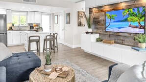 A modern living room with a large TV, grey sofas, a coffee table with decorative items, and a kitchen in the background. - Key Largo Kawama Villa L1, 3/3 (Key Largo)