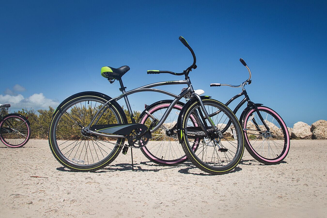 Two bicycles parked on a sandy beach with a clear sky.