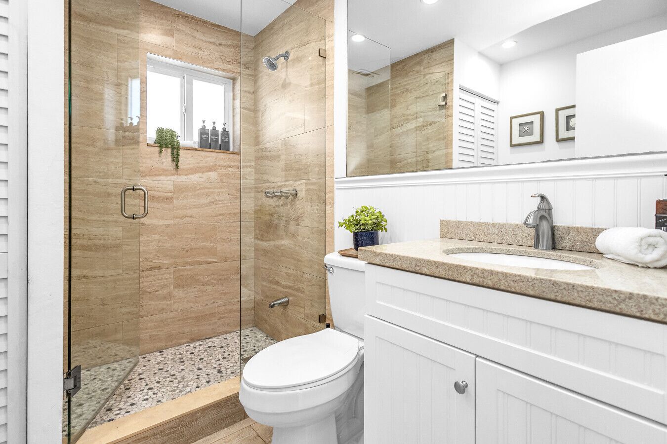 A modern bathroom with a glass-enclosed shower, a white toilet, a granite countertop, and a mirror above the sink.