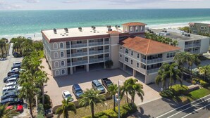 A multi-story hotel with a beach view, parking lot, and palm trees.