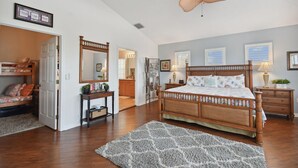 A bedroom with a large bed, a ceiling fan, a wooden dresser, a nightstand, and a mirror.