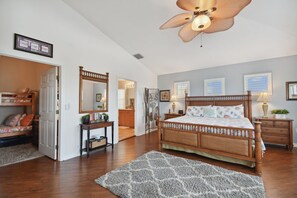 A bedroom with a large bed, a ceiling fan, a wooden dresser, a nightstand, and a mirror.