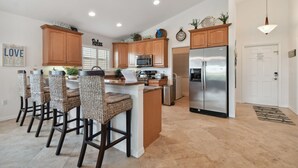 A modern kitchen with wooden cabinets, a central island with bar stools, stainless steel appliances, and decorative items on the walls.