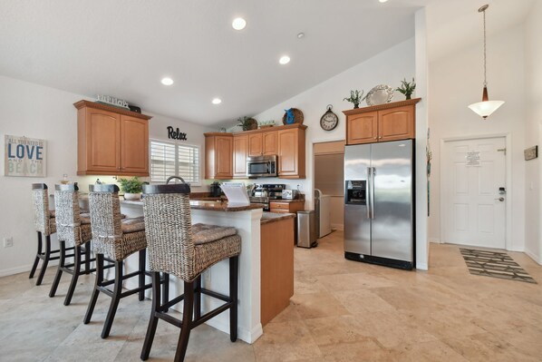 A modern kitchen with wooden cabinets, a central island with bar stools, stainless steel appliances, and decorative items on the walls.
