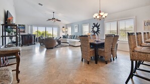 A spacious living area with a dining table, wicker chairs, a white sofa, and a ceiling fan.
