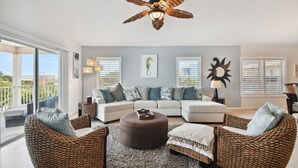 A spacious living room with a large sectional sofa, two wicker chairs, a round ottoman, and a ceiling fan.