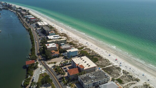 An aerial view of a coastal area with a beach, buildings, and a road.