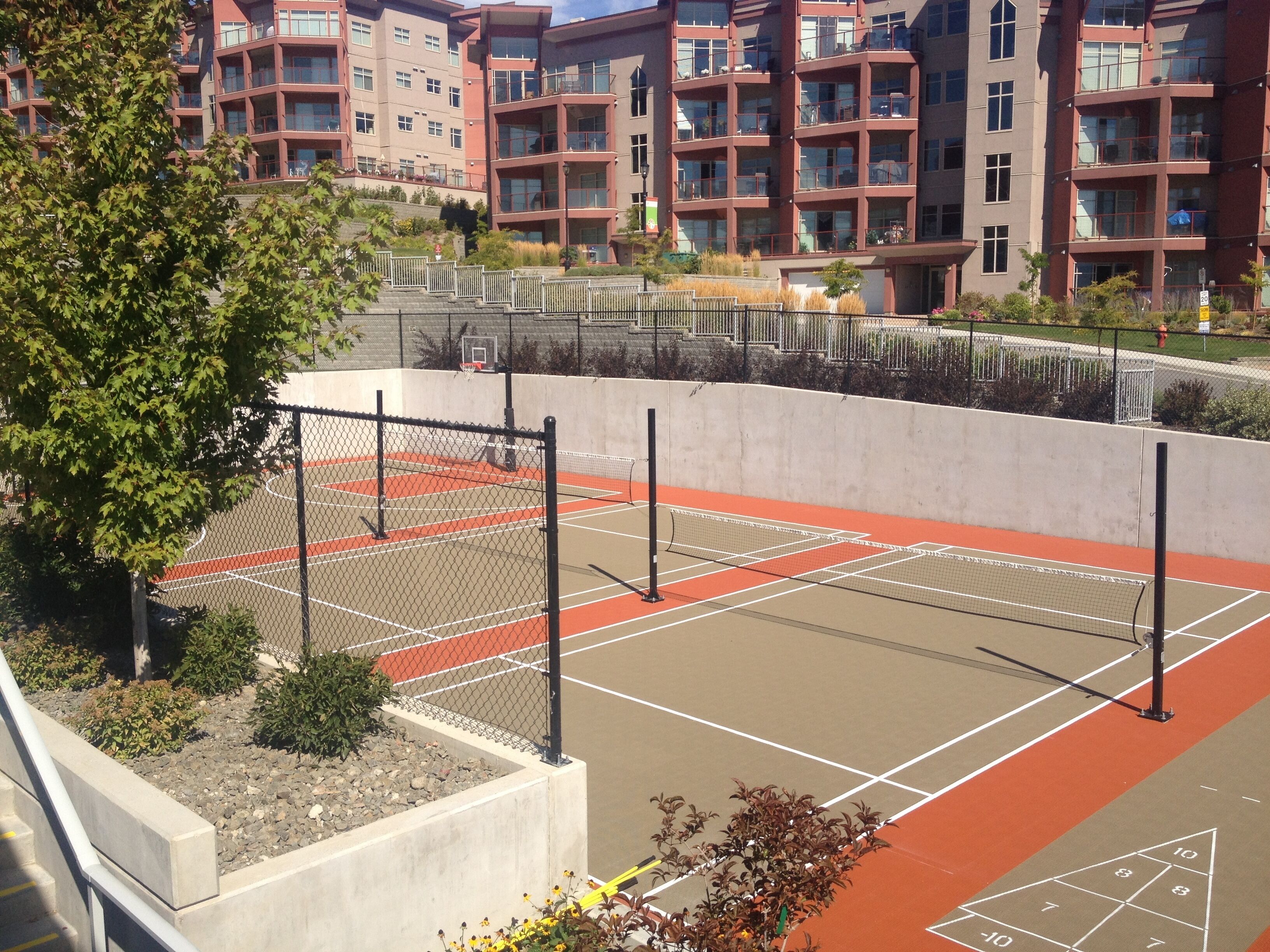 Una cancha de tenis con red, rodeada por una cerca y adyacente a un edificio con varios balcones.