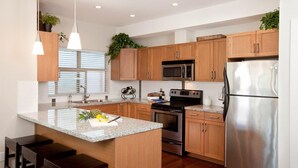A modern kitchen with wooden cabinets, stainless steel appliances, a granite countertop, and bar stools. - Lake View! Resort Style living. Short term rentals are allowed  at this complex. (Westbank, Kelowna)